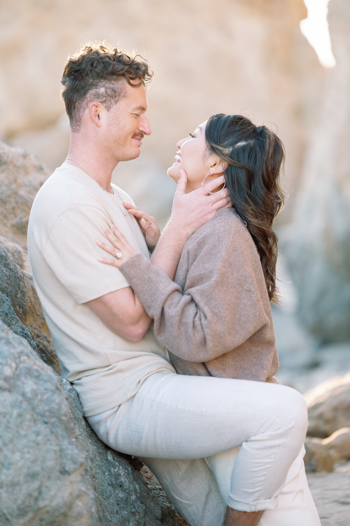 A man leaning on a rock as his partner leans in to kiss them