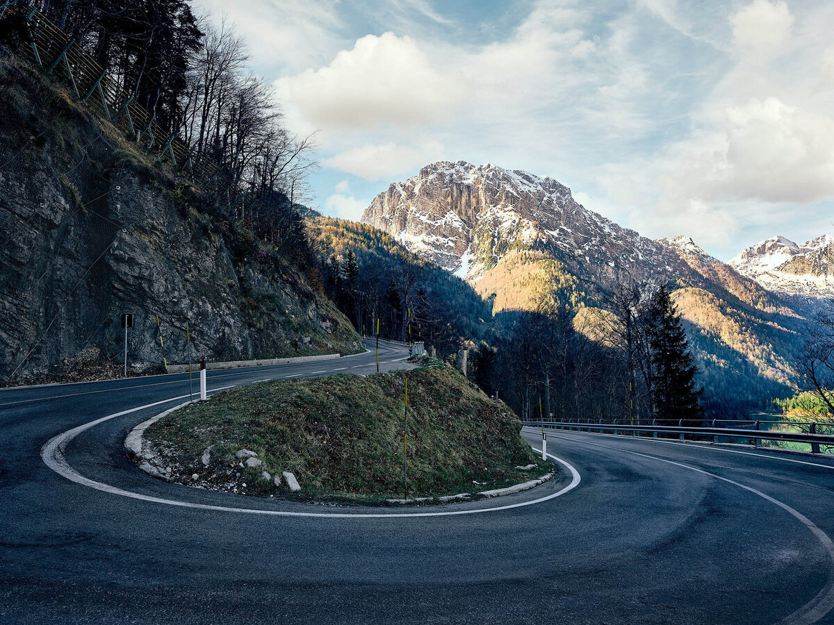 Fotografie einer kurvigen Passstraße in den italienischen Alpen – eindrucksvolle Landschaftsaufnahme mit Blick auf schneebedeckte Gipfel von Fotograf Atelier Schulte.