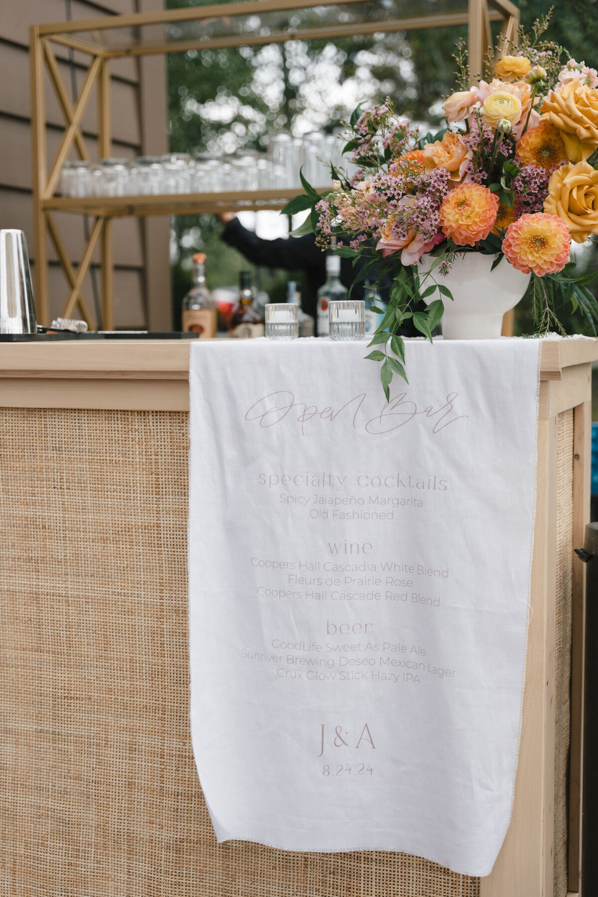 custom calligraphy bar menu on linen hanging from a rattan tabletop with florals representing full service design and calligraphy by Life in Letters.