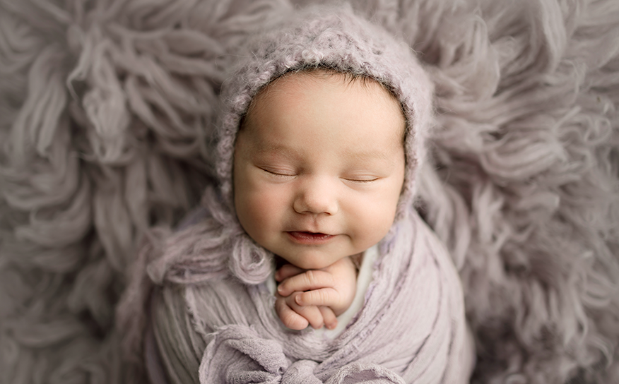 Newborn baby girl on a purple rug with a matching bonnet