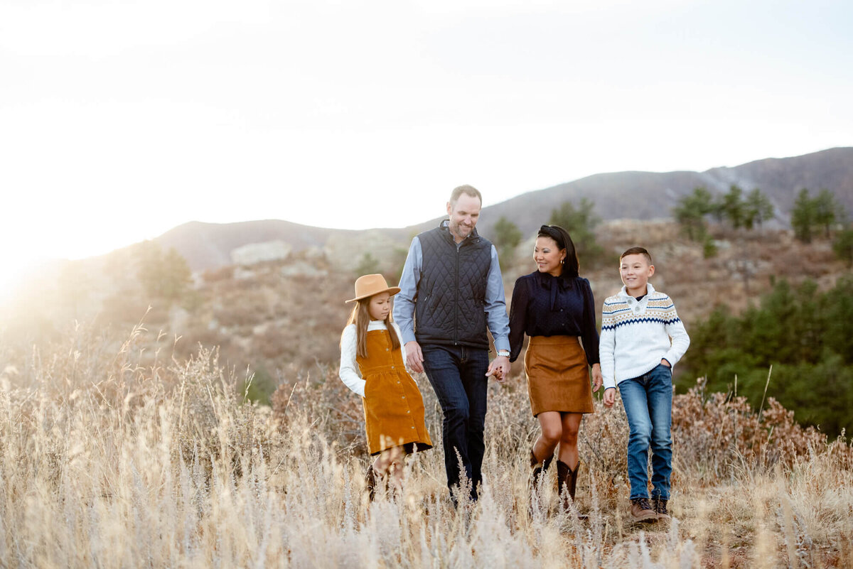 A family of 4 walk together holding hands on a trail at sunset