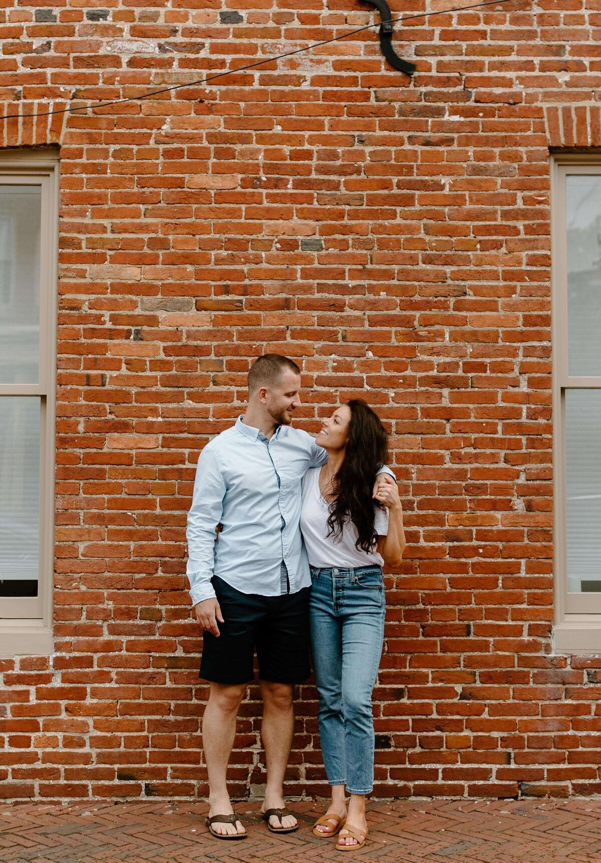 man puts arm around woman during engagement session in front of brick wall in baltimore maryland