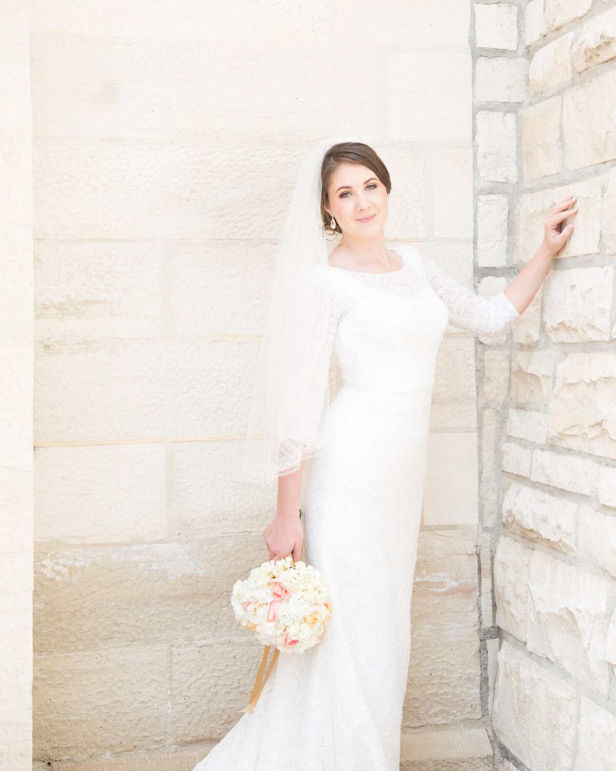 bride in a classic beaded dress and veil  against stone wall