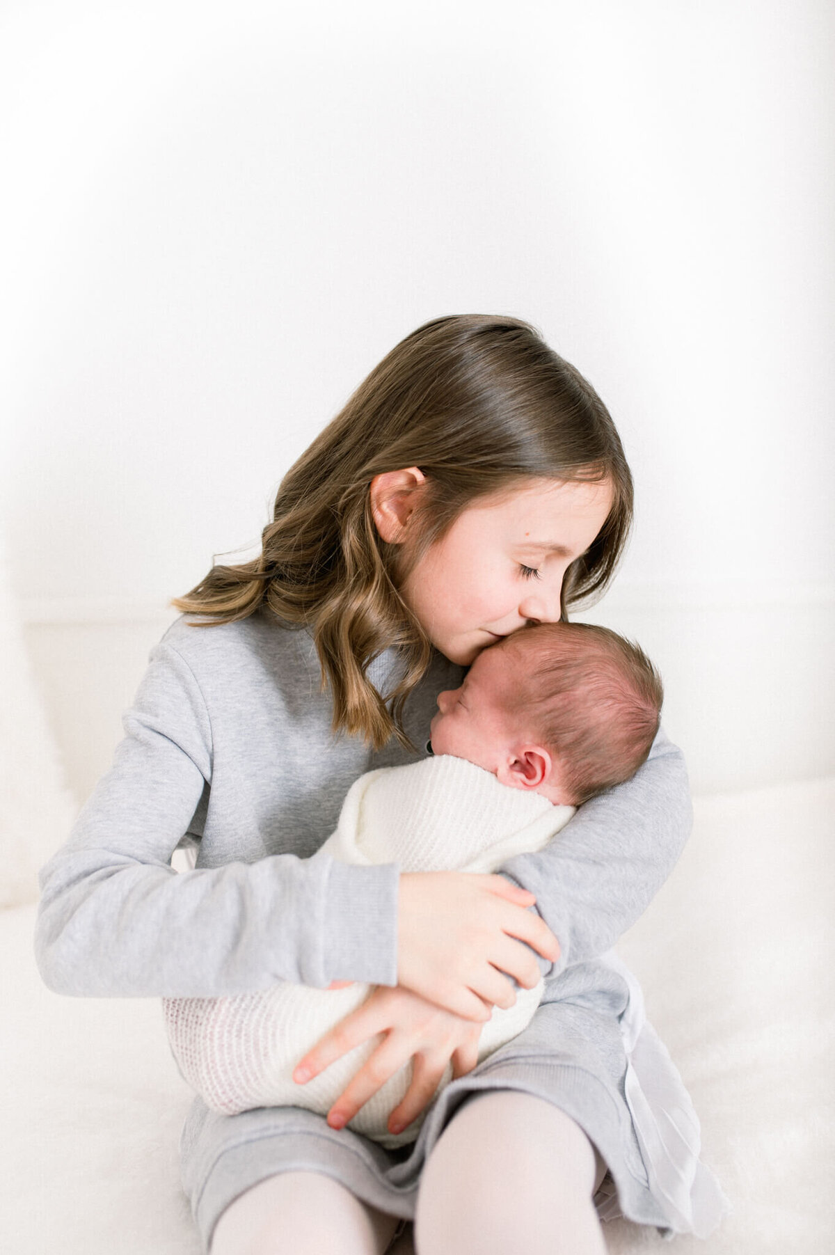 Big sister kisses baby brother on head. Captured by Niagara Newborn Photographer