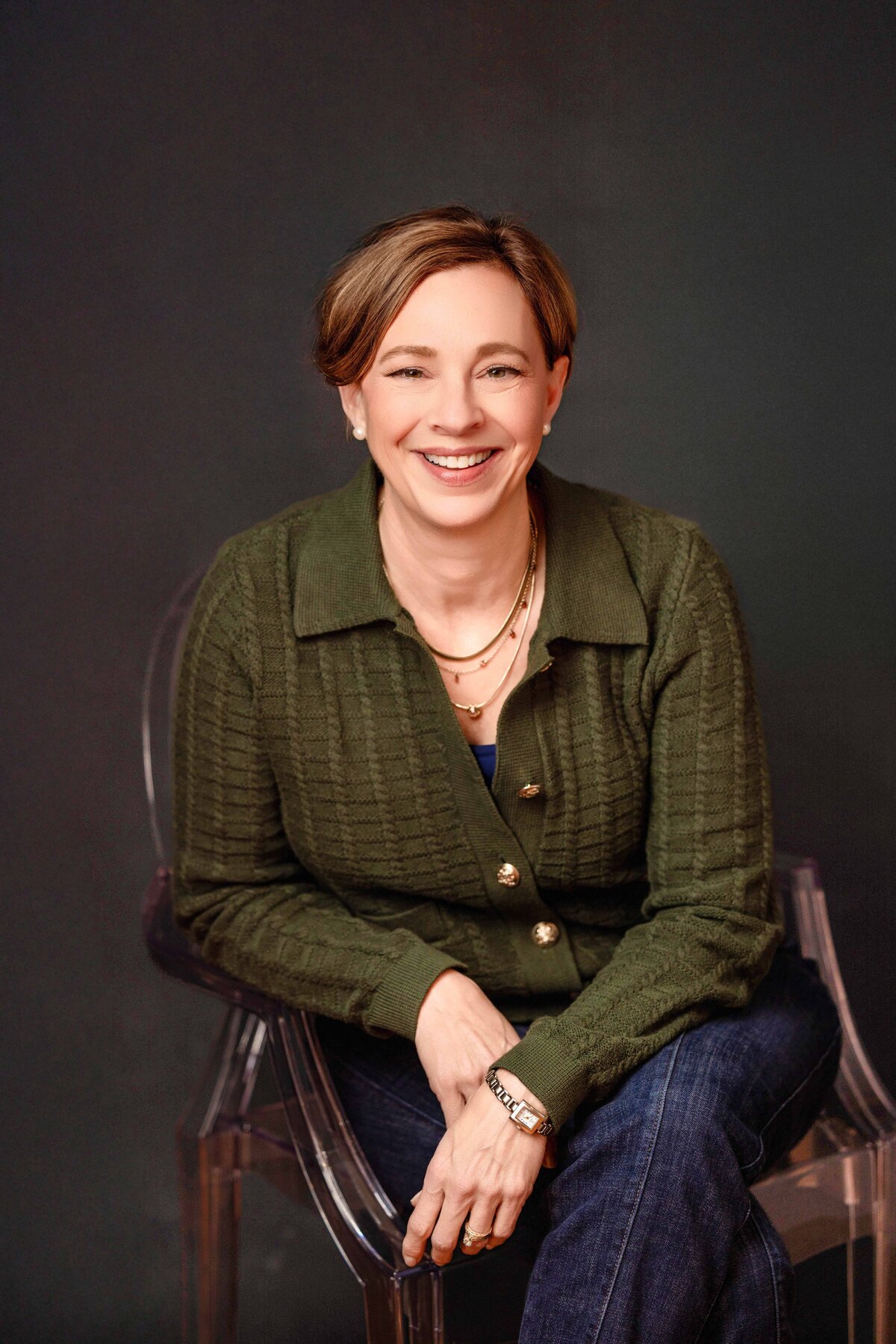 Studio branding headshot of a woman in a green blazer, seated confidently with a warm smile.