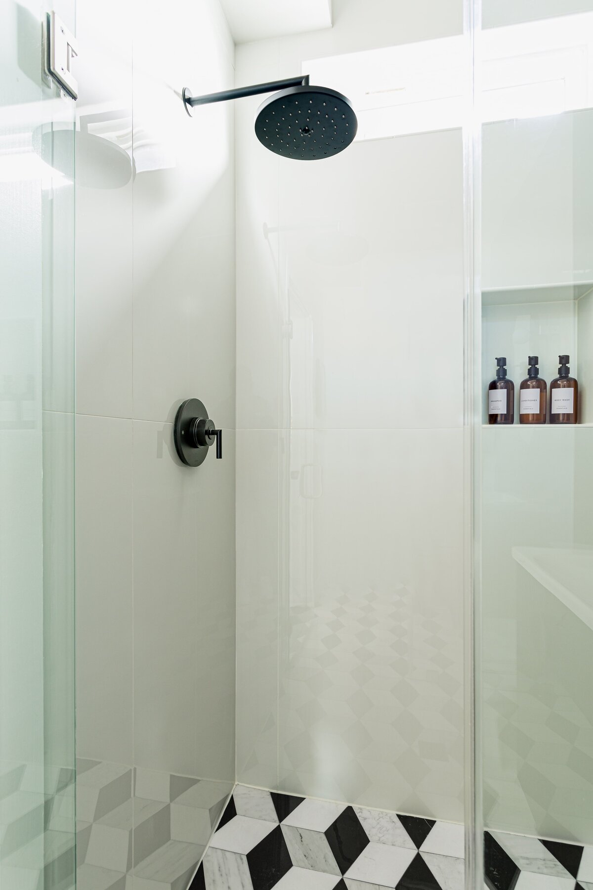 Minimalist bathroom shower featuring a sleek glass enclosure, modern showerhead, and a small shelf holding toiletries