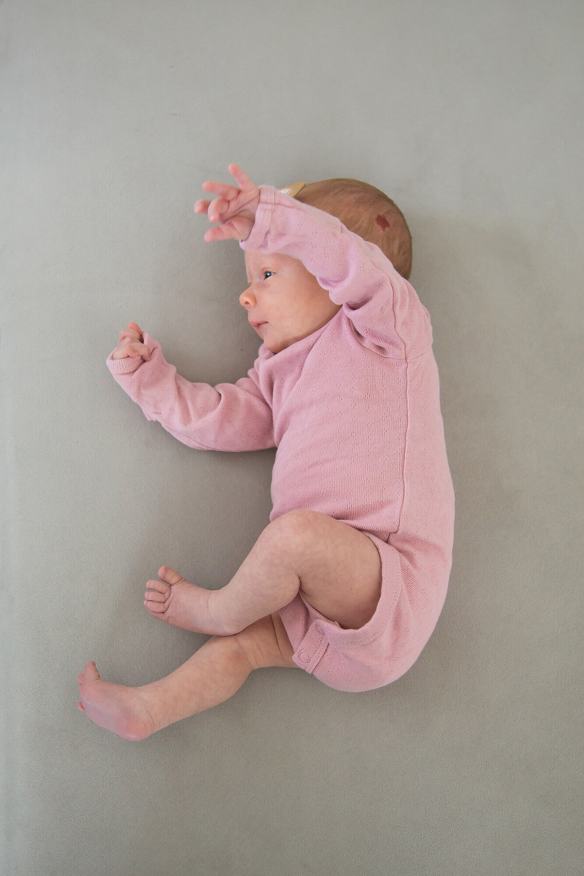 View from above of newborn baby girl stretching arms and legs in front of her