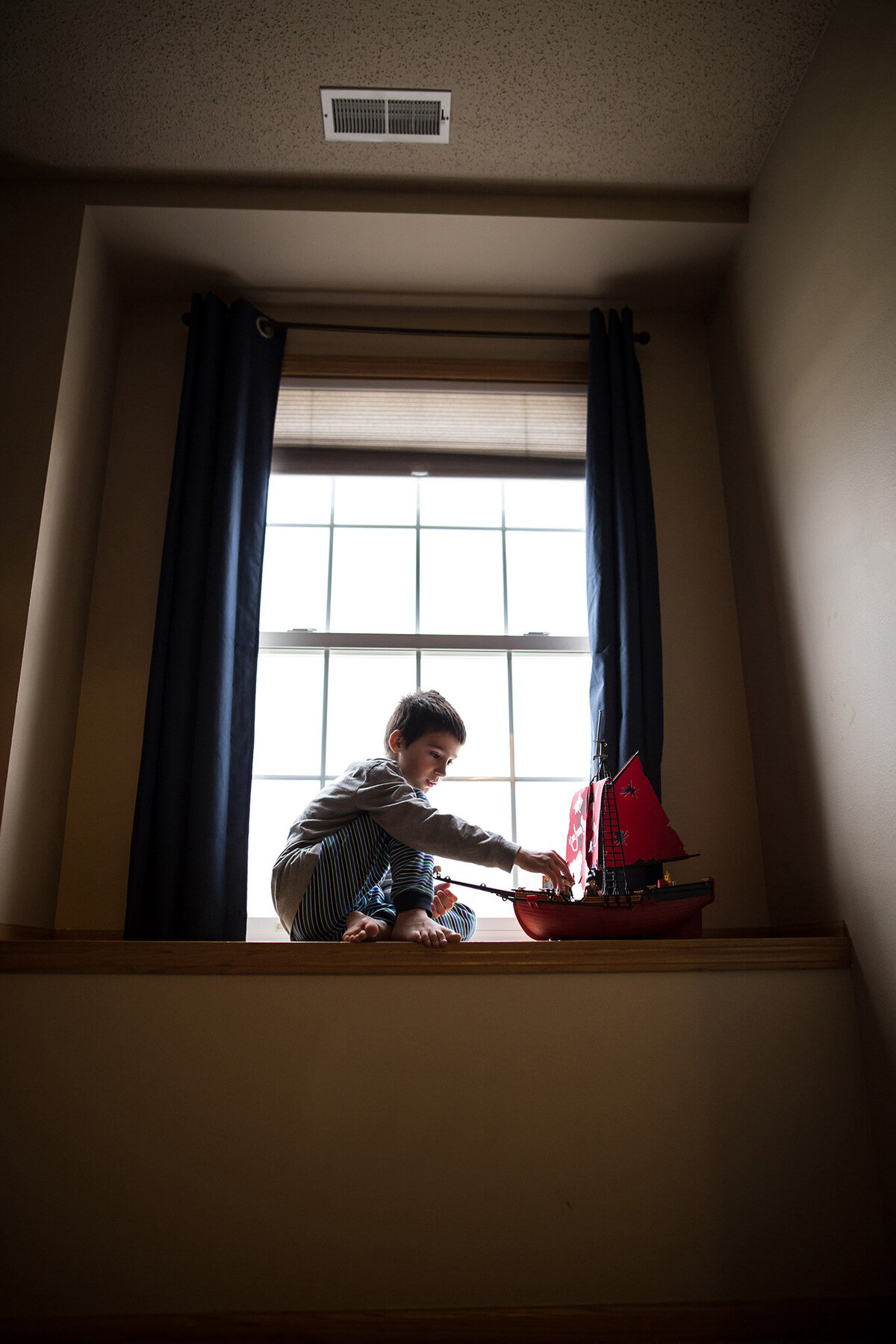 little boy playing with pirate ship in window sill