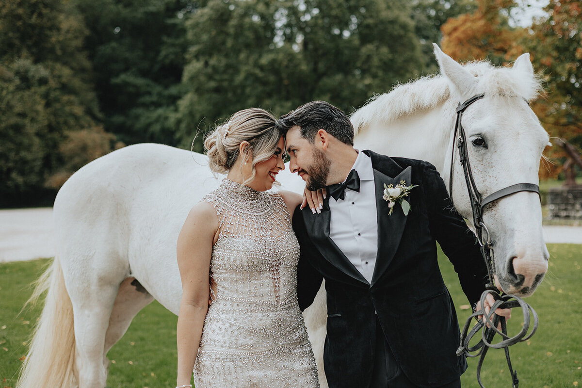 Bride and groom forehead to forehead in front of a white horse