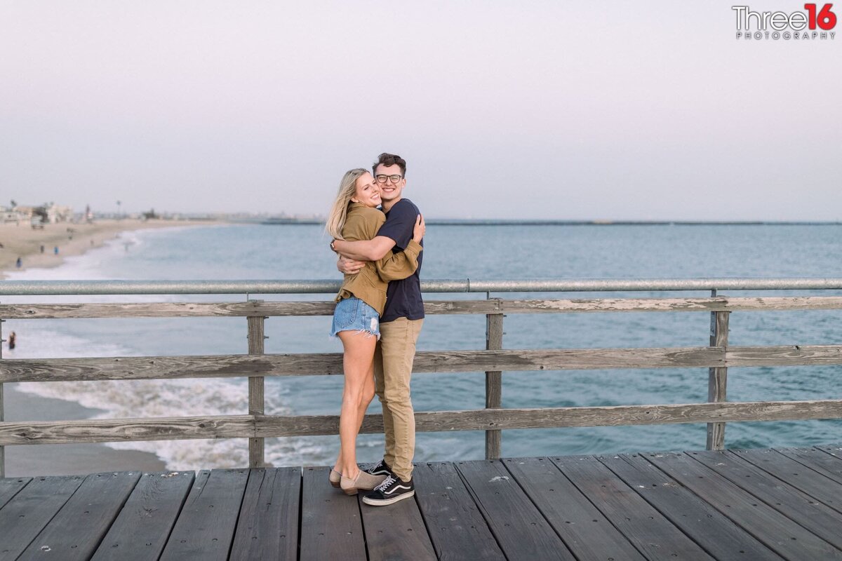 Sweet embrace by engaged couple on the boardwalk of the Seal Beach Pier