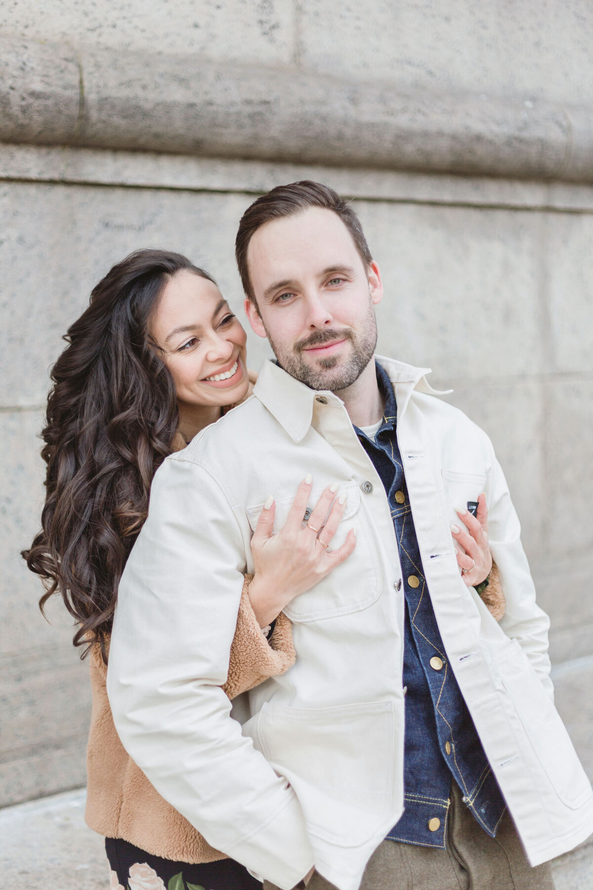 An engaged couple cuddle by the Boston Public Library