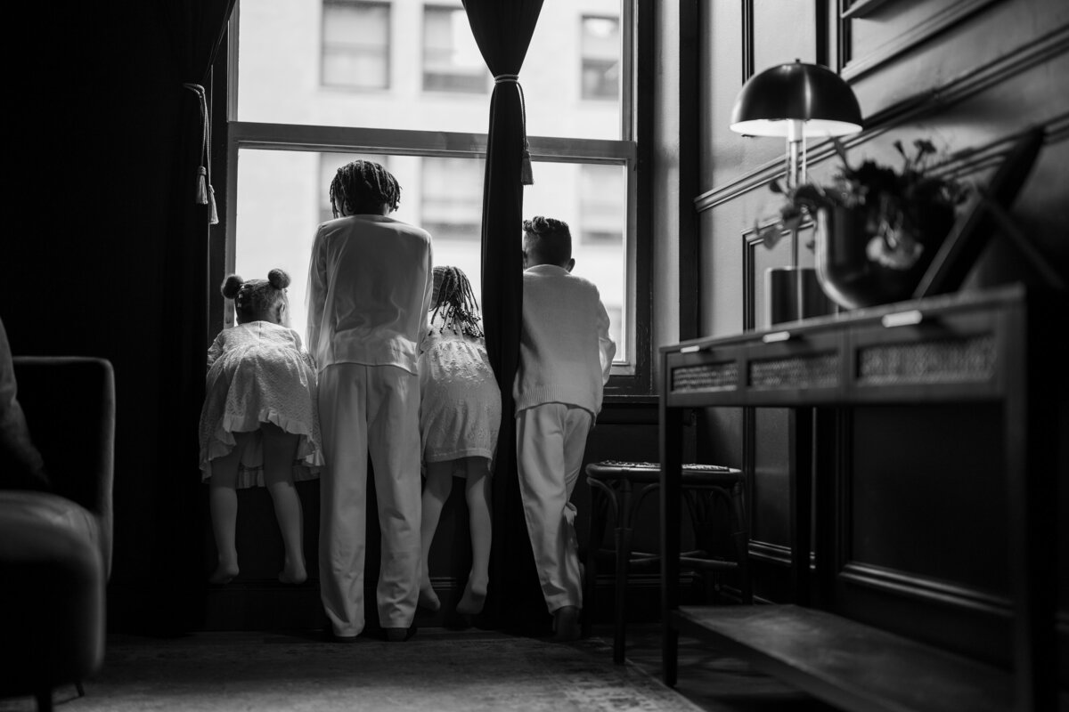 A timeless black-and-white photo of siblings gathered by the window, evoking nostalgia and connection in a family session in NYC.