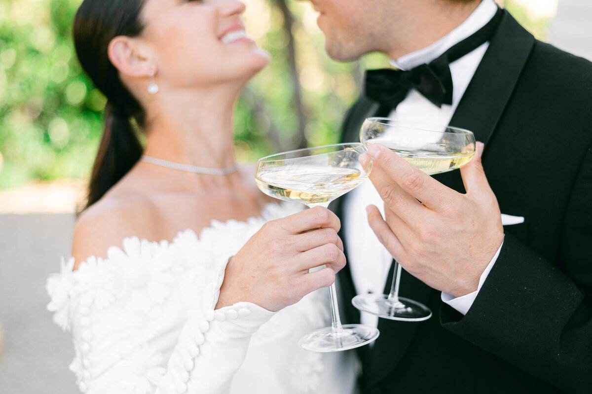 Elegant bride and groom smile while drinking champagne from coups
