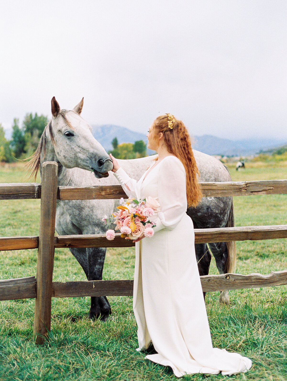 Bride caresses horse as she leans over the fence