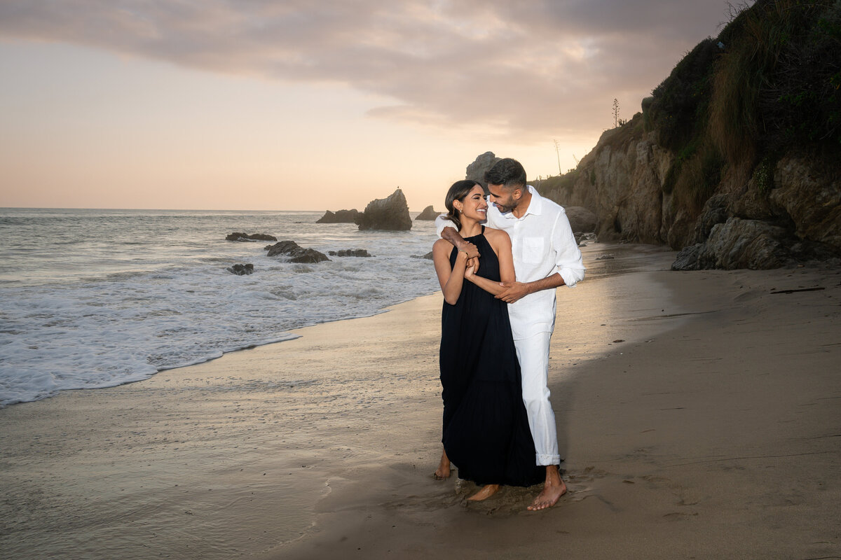 Indian couple eloping at El Matador State Beach in Malibu during low-tide sunset embracing.