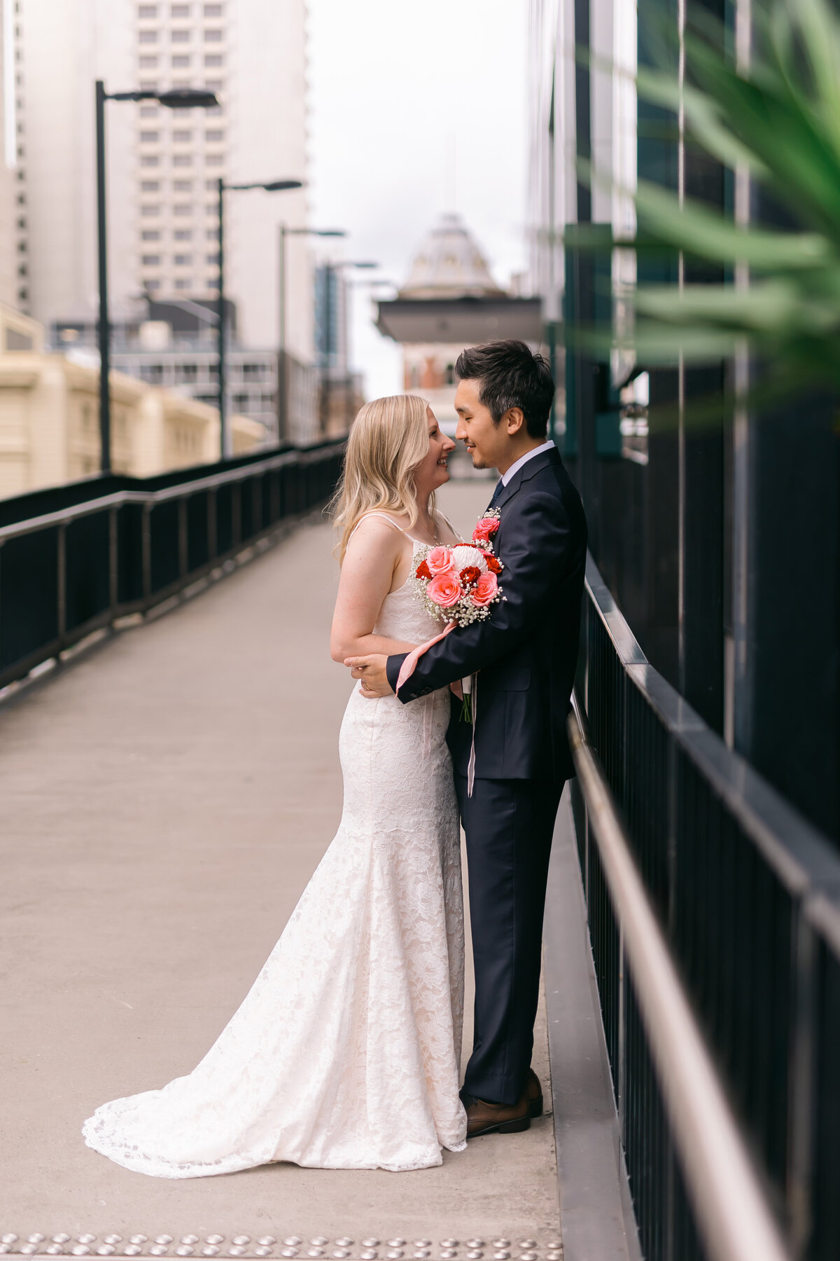 Bride and groom sharing a kiss on a high-rise balcony near the Brisbane Registry Office, with city buildings behind them.