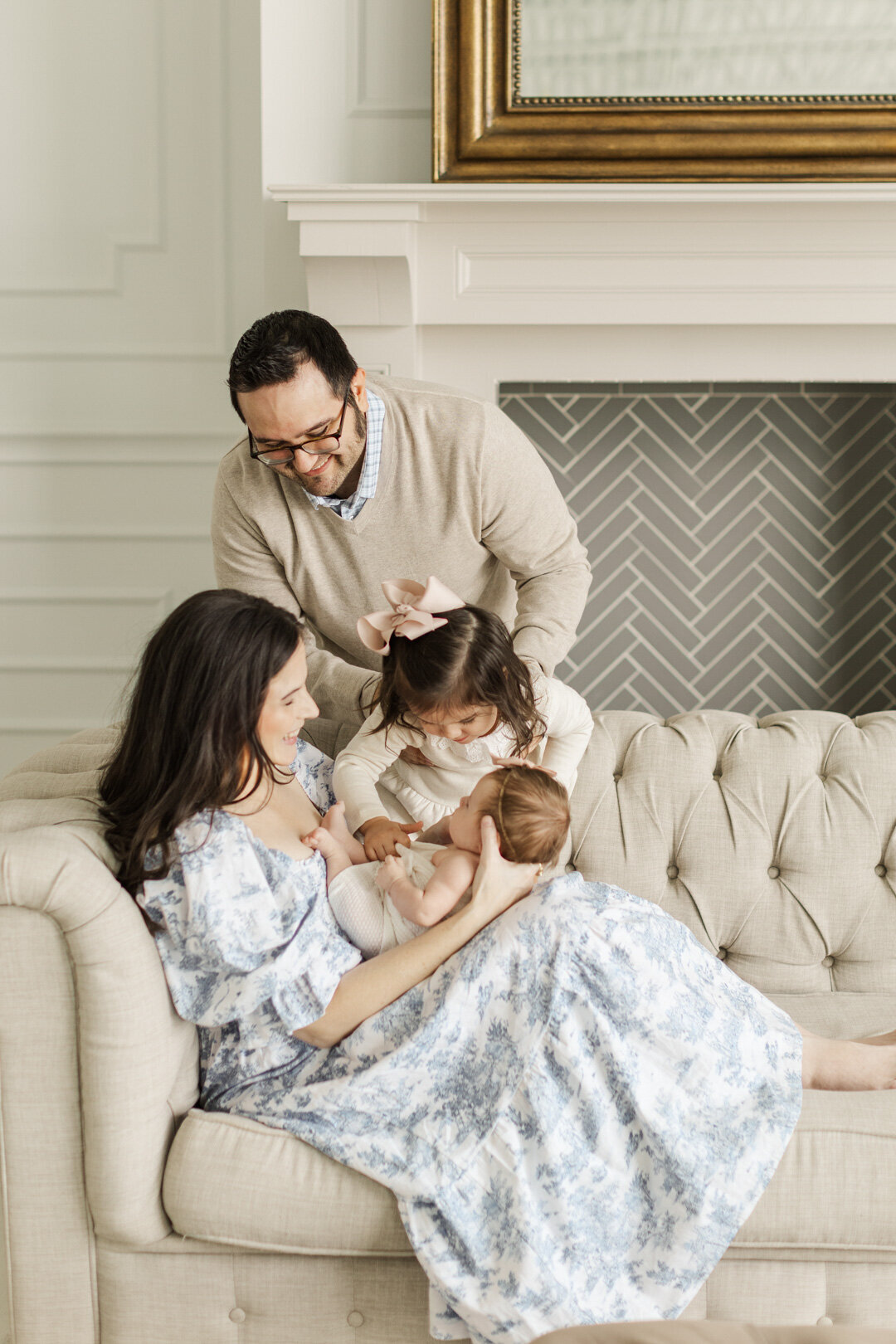 dad holds big sister over newborn baby and mom sitting on sofa for katy newborn photographer