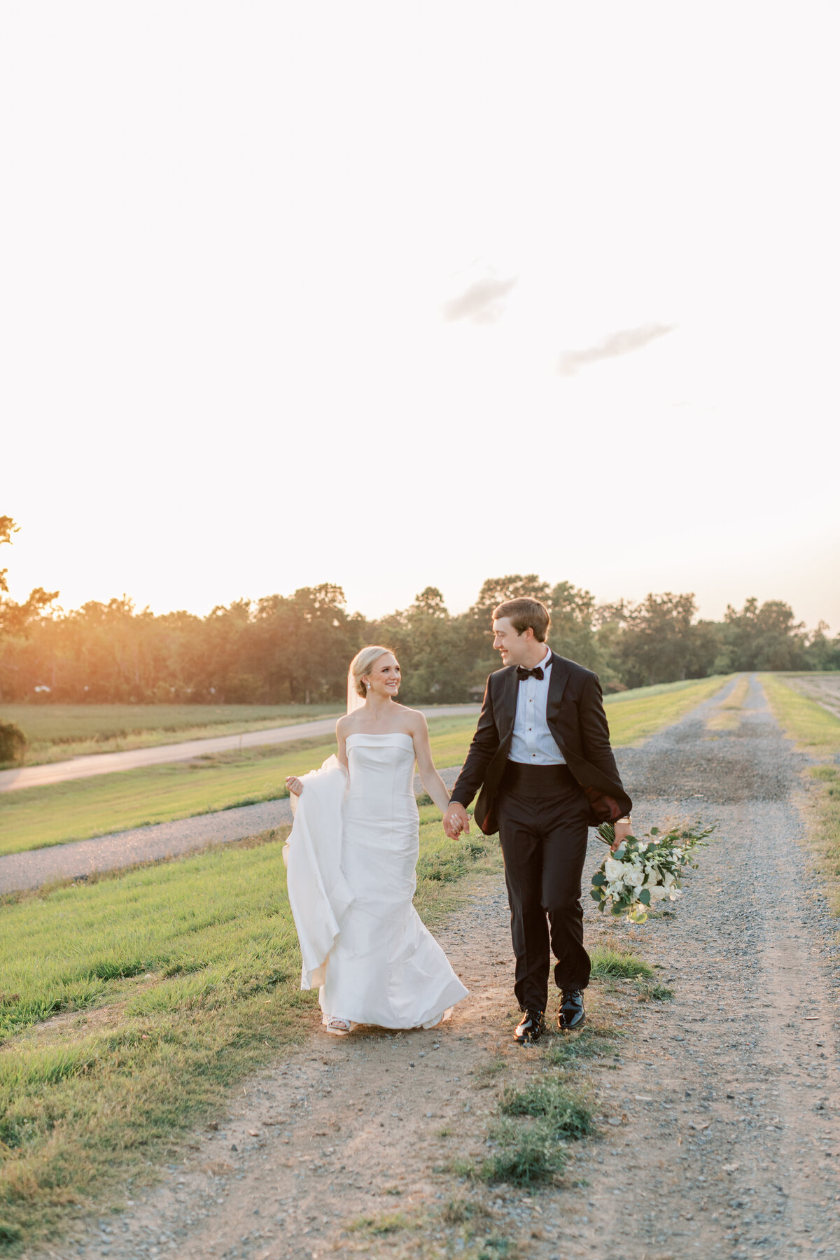 A husband and wife walk hand in hand with the sunset behind them.
