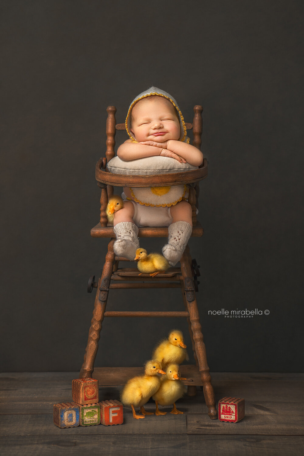Newborn baby sleeping and smiling in doll high chair with baby ducklings.