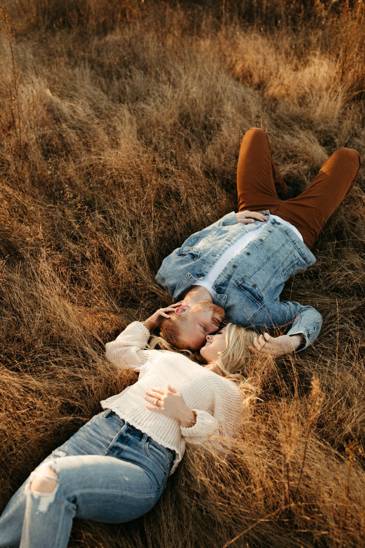 Couple laying down in a grassy field face to face at sunset