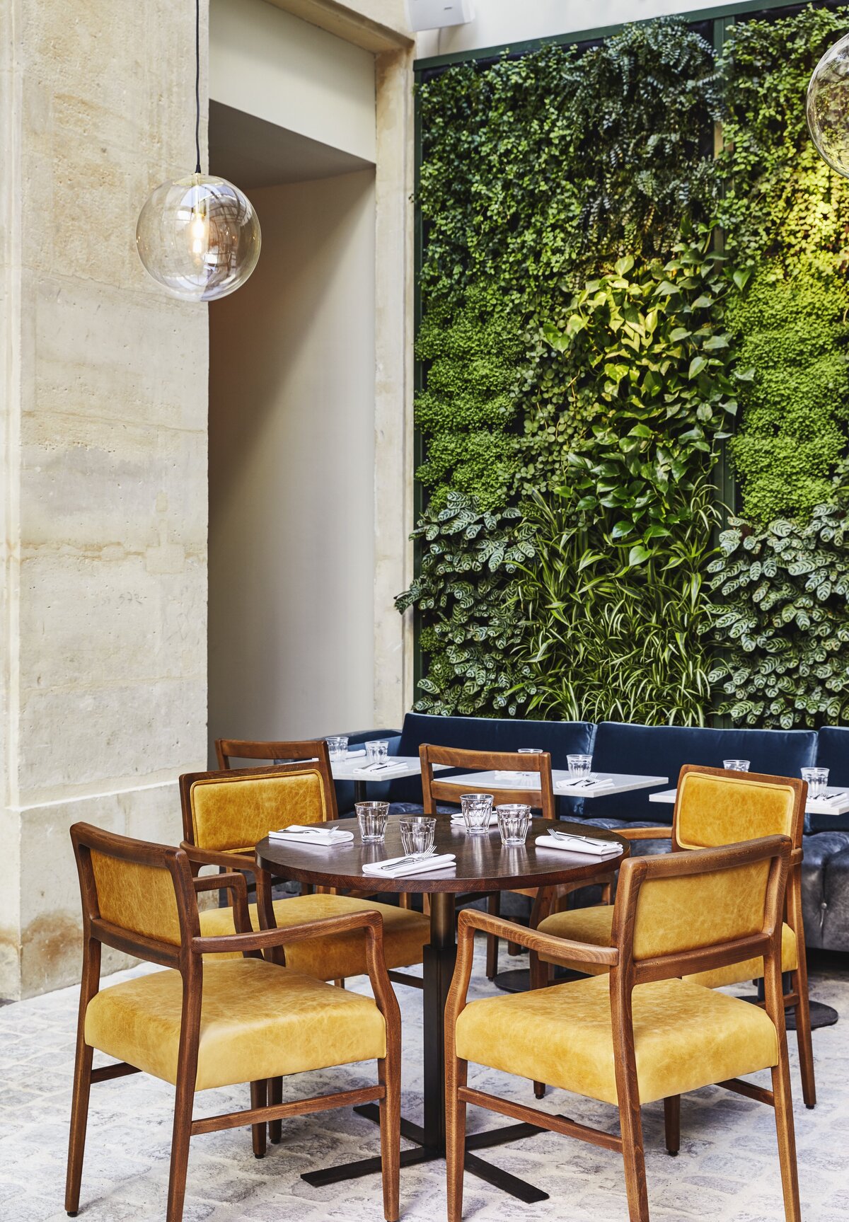 Restaurant with wooden table and wooden dining chairs with mustard colored leather upholstery. Green wall and limestone in the background