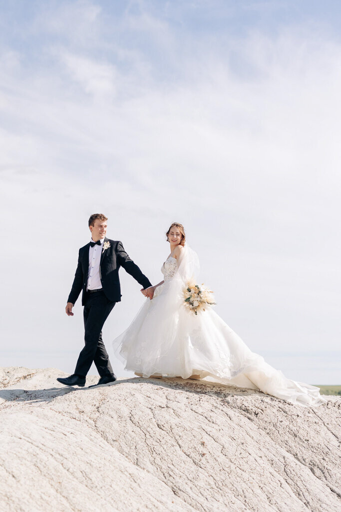 Bride and groom walk along rocks with beautiful blue sky in background,  captured by Lorissa Lee Photography. Featured on Brontë Bride.