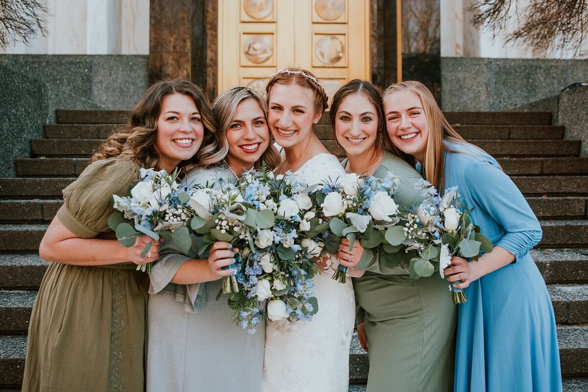 A group of four bridesmaids holding bouquets smiles with the bride