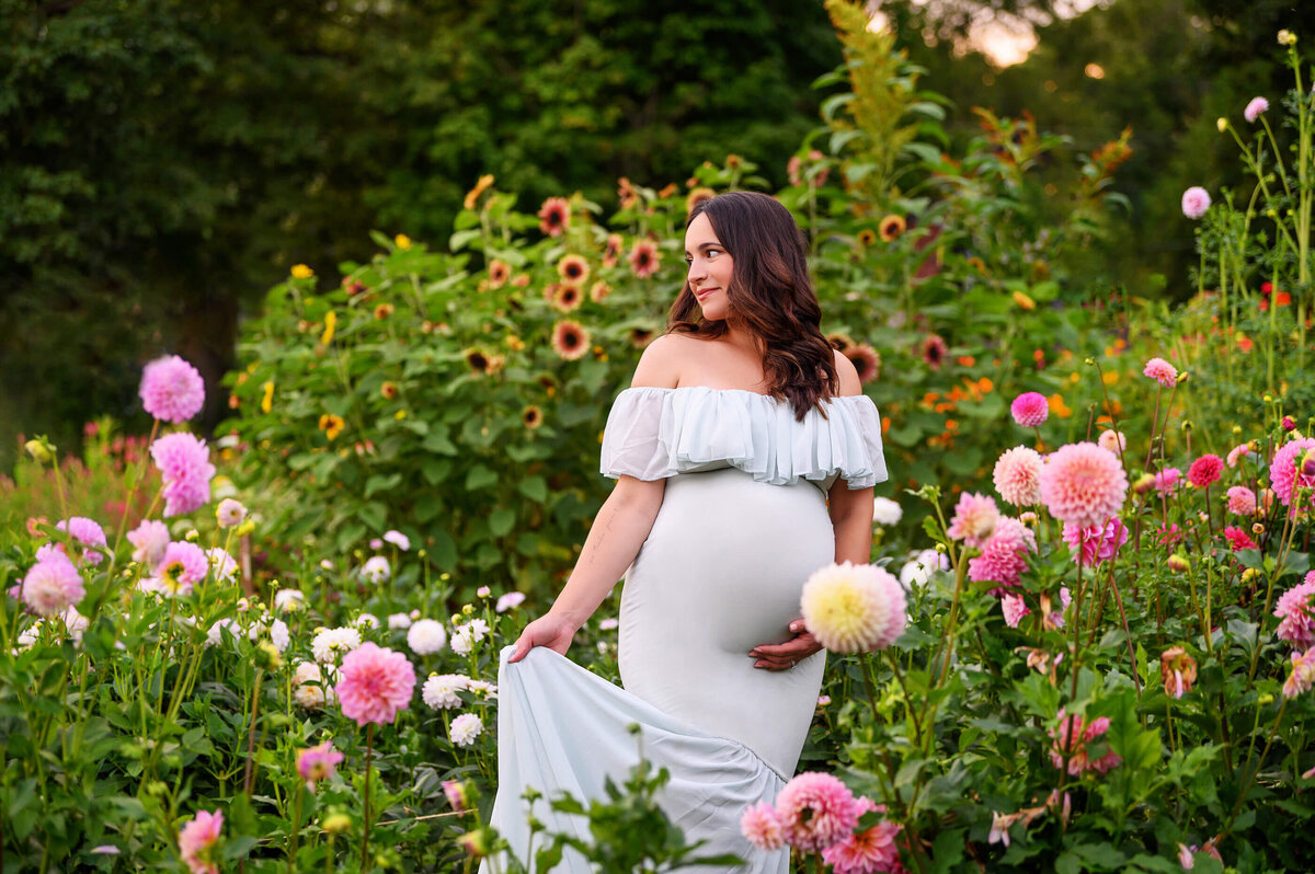 Pregnant woman wearing a mint green dress in a flower field holding her belly for her Burlington, Ontario outdoor maternity photography session