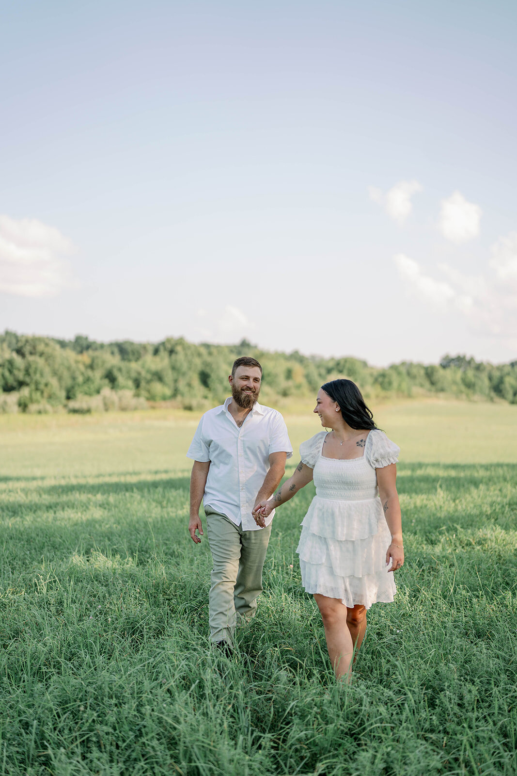 Kali and Joe walking together through a peaceful grassy field during their private property engagement session.
