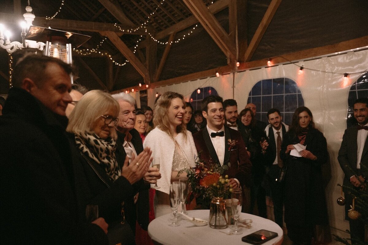 Mariés entourés de leurs invités sous une tente éclairée, sourire aux lèvres. Photo Kamescop, vidéaste et photographe de mariage en Bretagne.