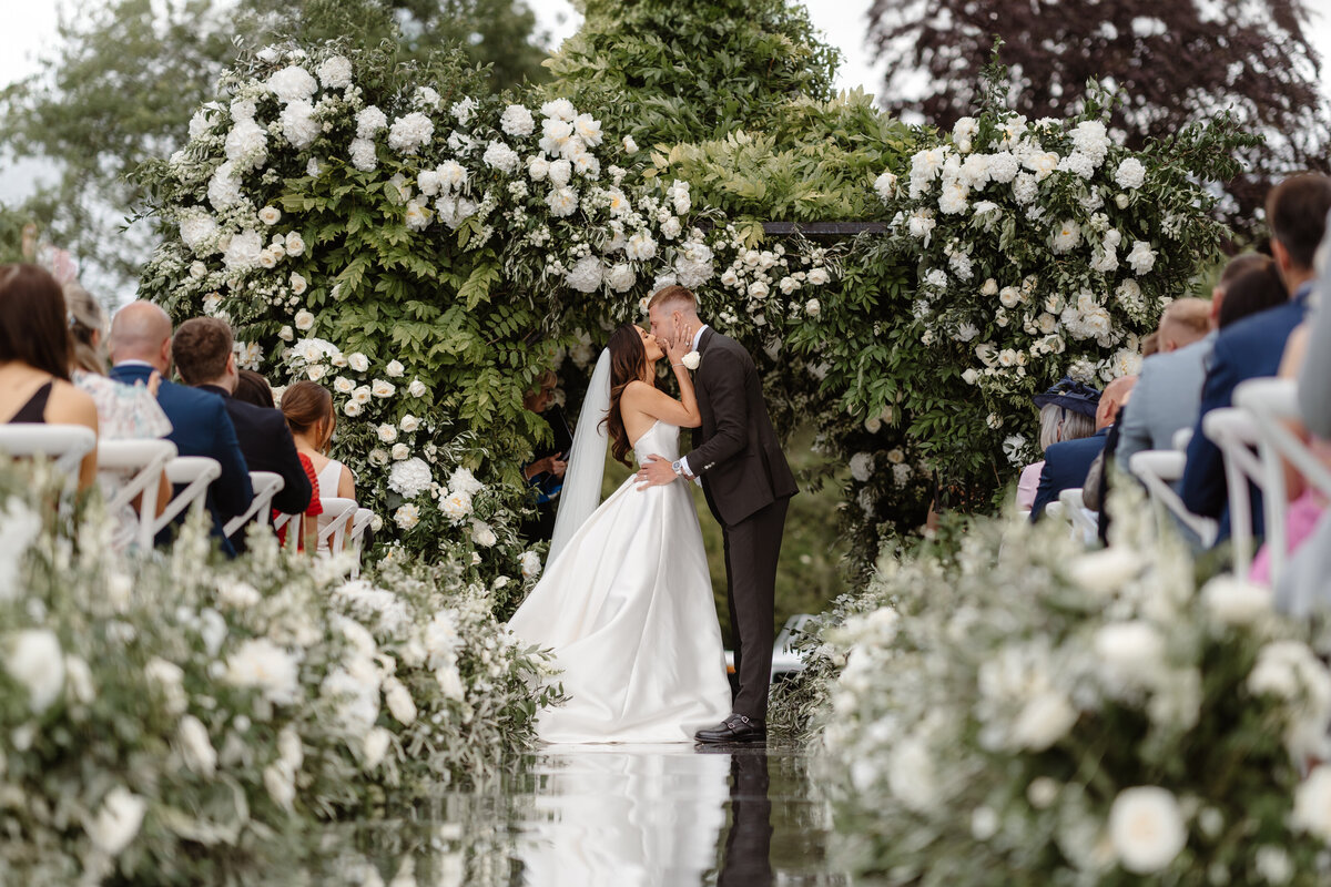 Monkey Island Estate outdoor ceremony with large floral backdrop and mirror aisle