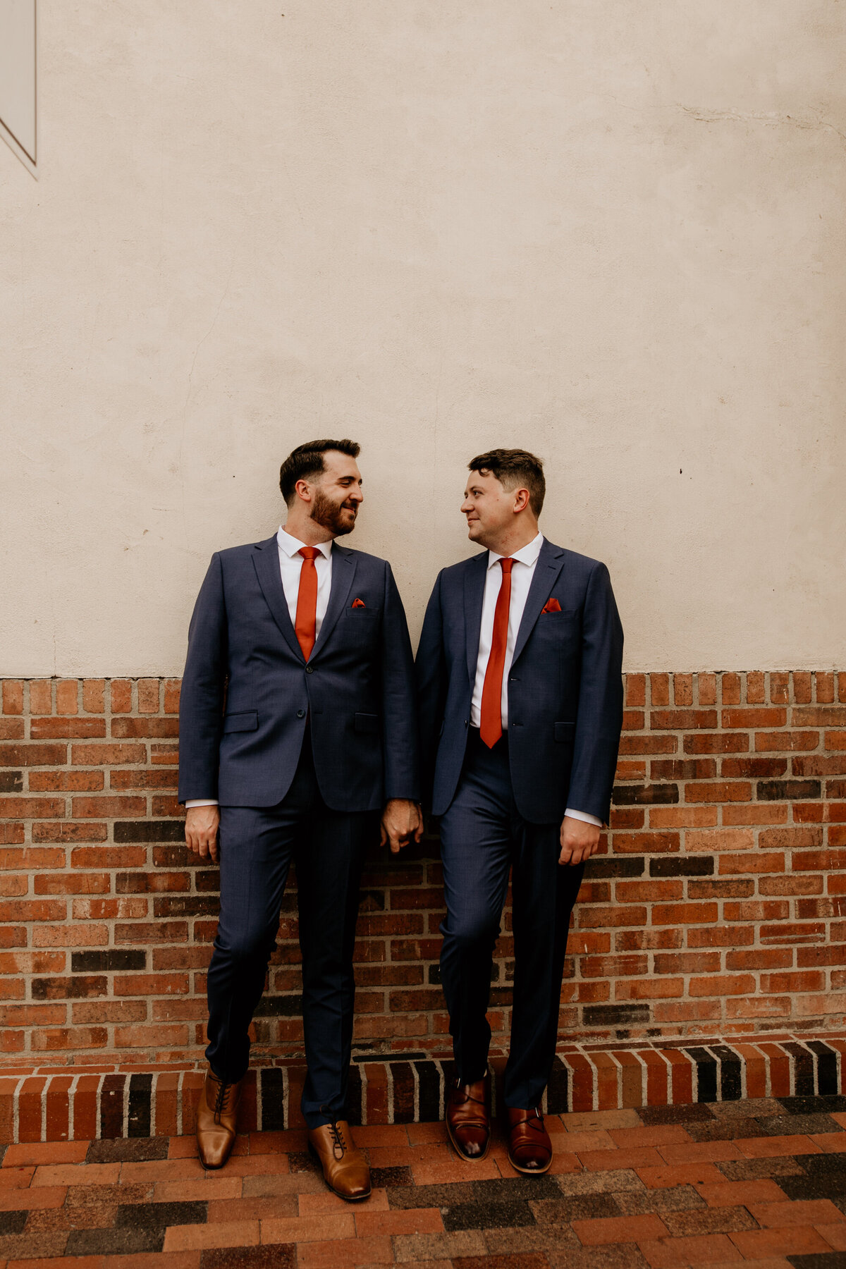 two grooms standing against a building holding hands in downtown Albuquerque