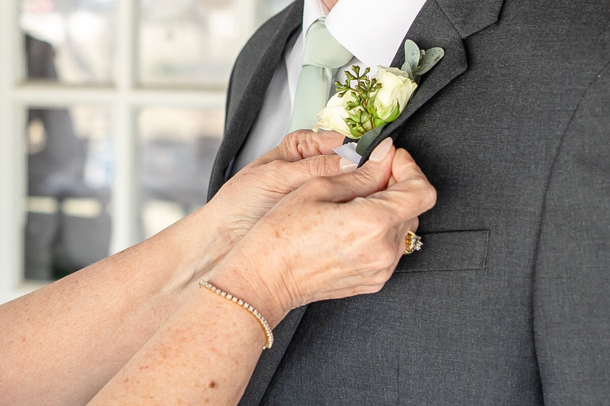 groom's mother pins boutonniere of white rose by Firefly Photography