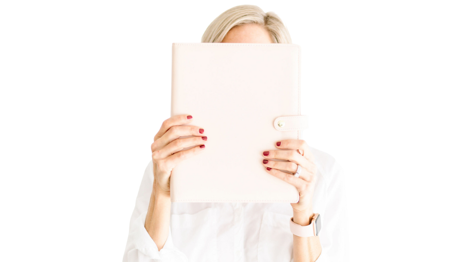 Woman hiding behind a paper planner she is holding