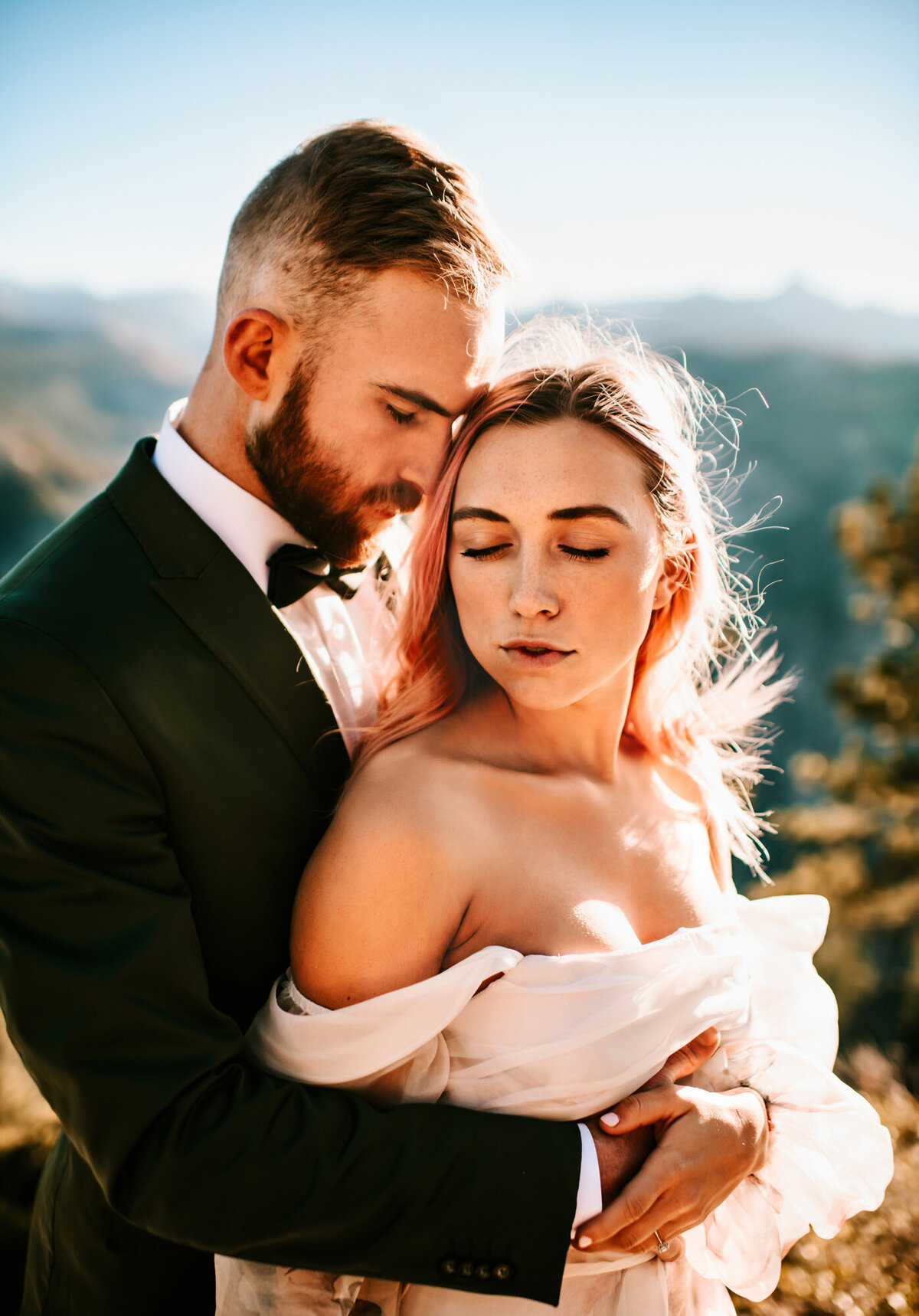Couples Photography, groom embraces bride from behind as they both savor their day , they are on a mountaintop