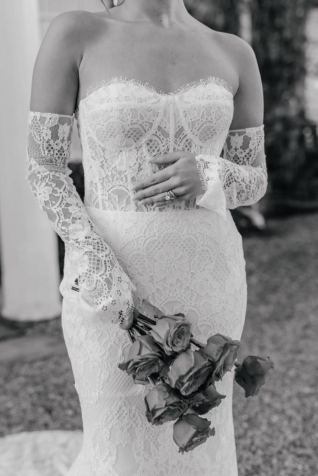 Close up lace detail wedding dress with brides hand gently placed on her chest showing her diamond wedding ring at Northbrook Park in Farnham