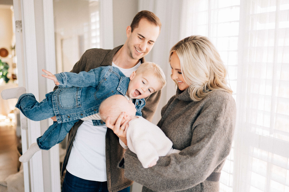 joyful photo of mom holding baby and dad lifting toddler toward baby