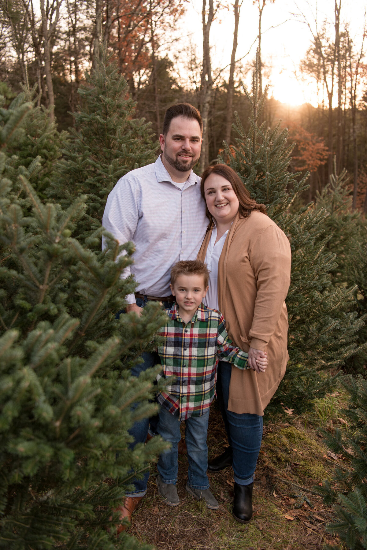 Mom, Dad, little boy smiling and looking at the camera with Christmas trees in the background