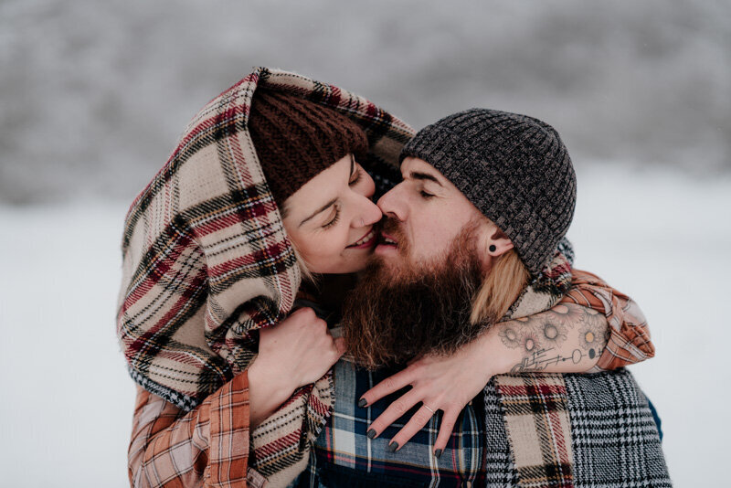 Couple enlacé sous une couverture dans un paysage enneigé de Haute-Savoie, moment d’intimité au cœur de l’hiver.