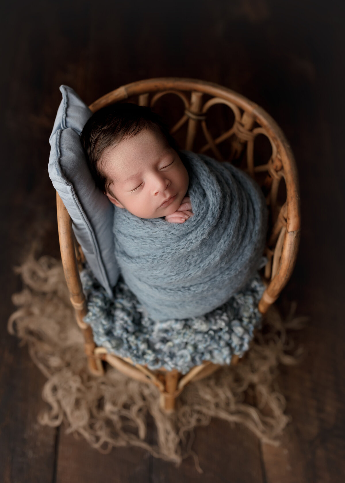 Newborn photoshoot with top Florida newborn photographer. Baby wrapped in a blue knit wrap with his hands peeking out of the wrap. Baby is sleeping.