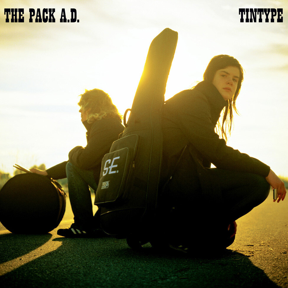 Album Cover Title Tintype Artist The Pack AD sitting on road with guitar and drum sun shining behind them