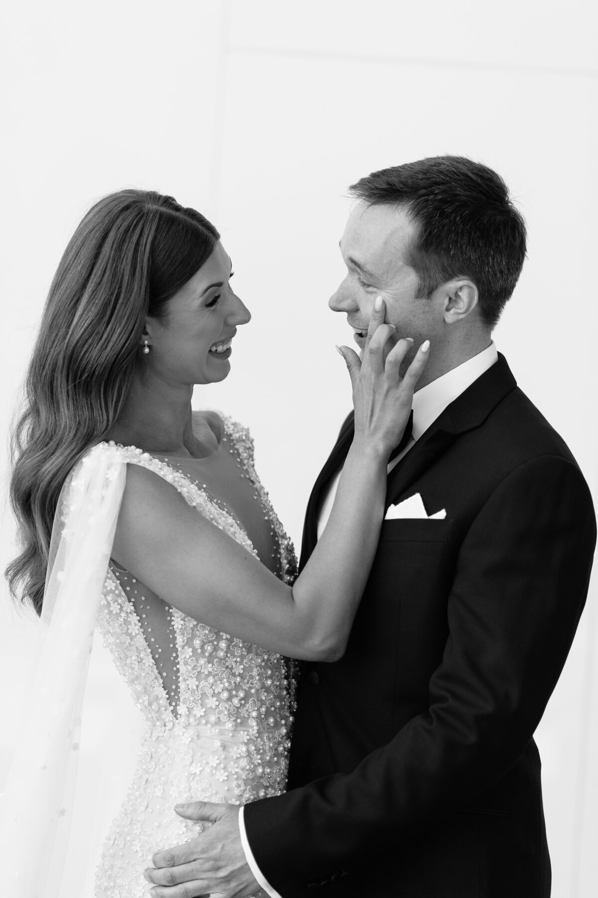 A bride and groom in black and white. The bride wipes the groom's tear from his cheek after he sees her for the first time on their wedding day.