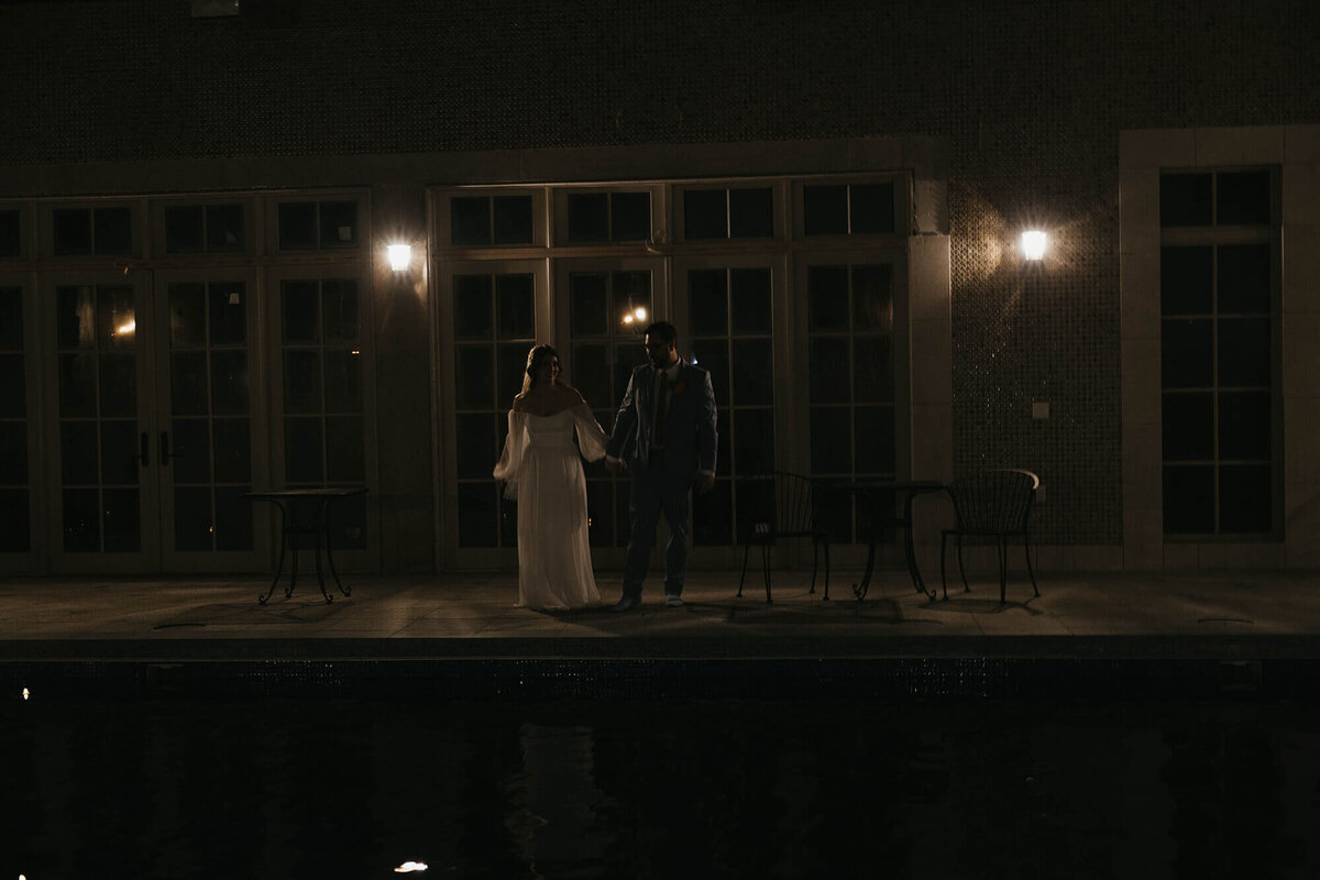 A bride and groom hold hands and stand at the edge of the outdoor pool at the Chateau de Lis in Oregon.