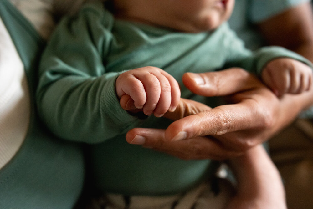 Infant grabbing dad's fingers green onesie