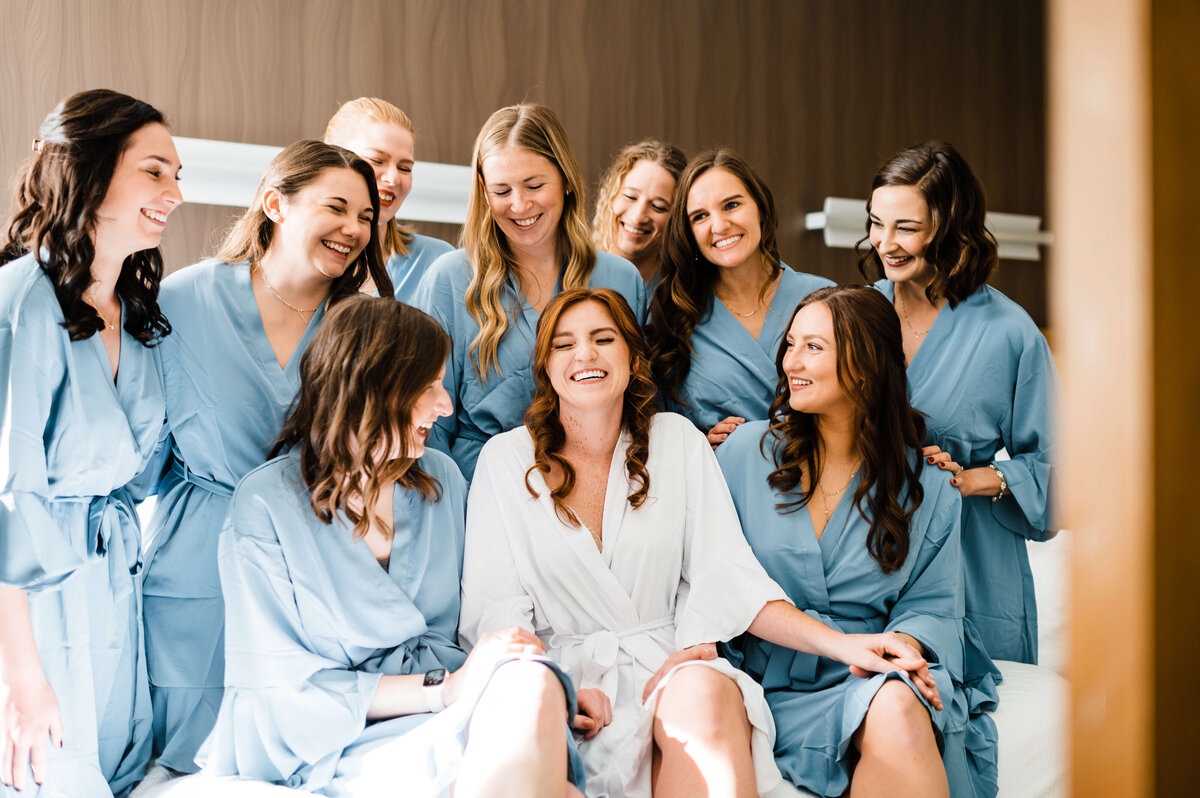 bride laughing with her bridesmaids the morning of her wedding as they are all in robes while getting ready