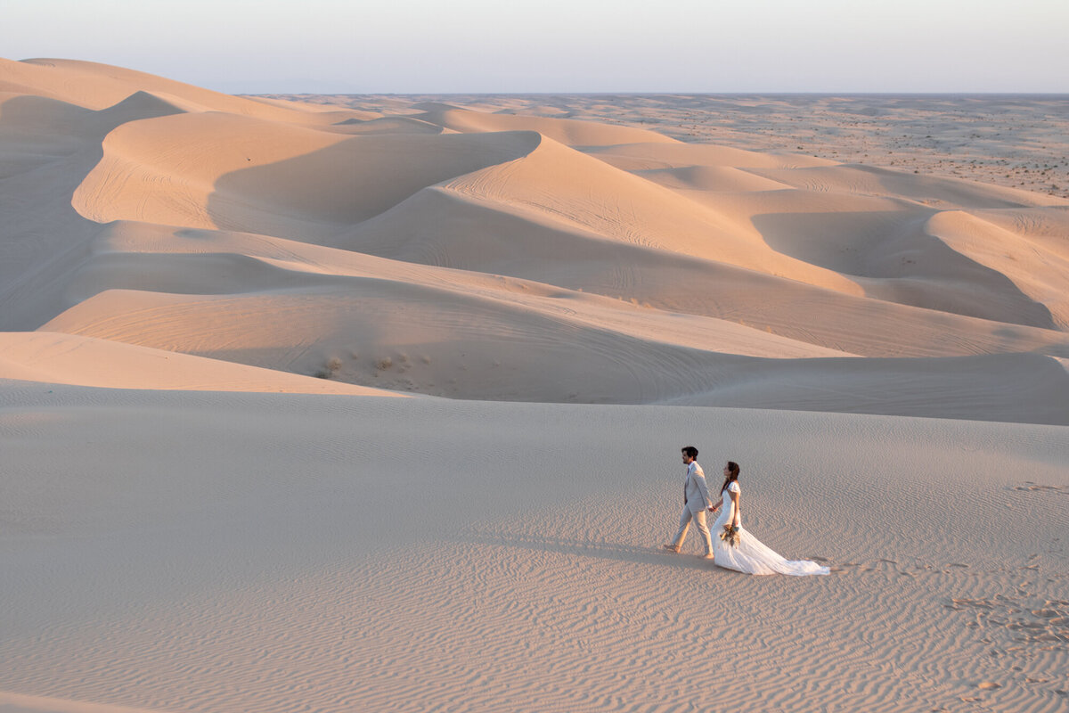 A bride and groom walk hand in hand across a sand dune on their California elopement day.