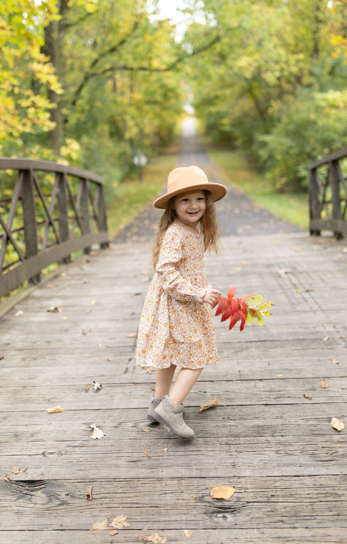 Little girl in hat holding fall leaves on wooden bridge - outdoor child portrait Maple Grove
