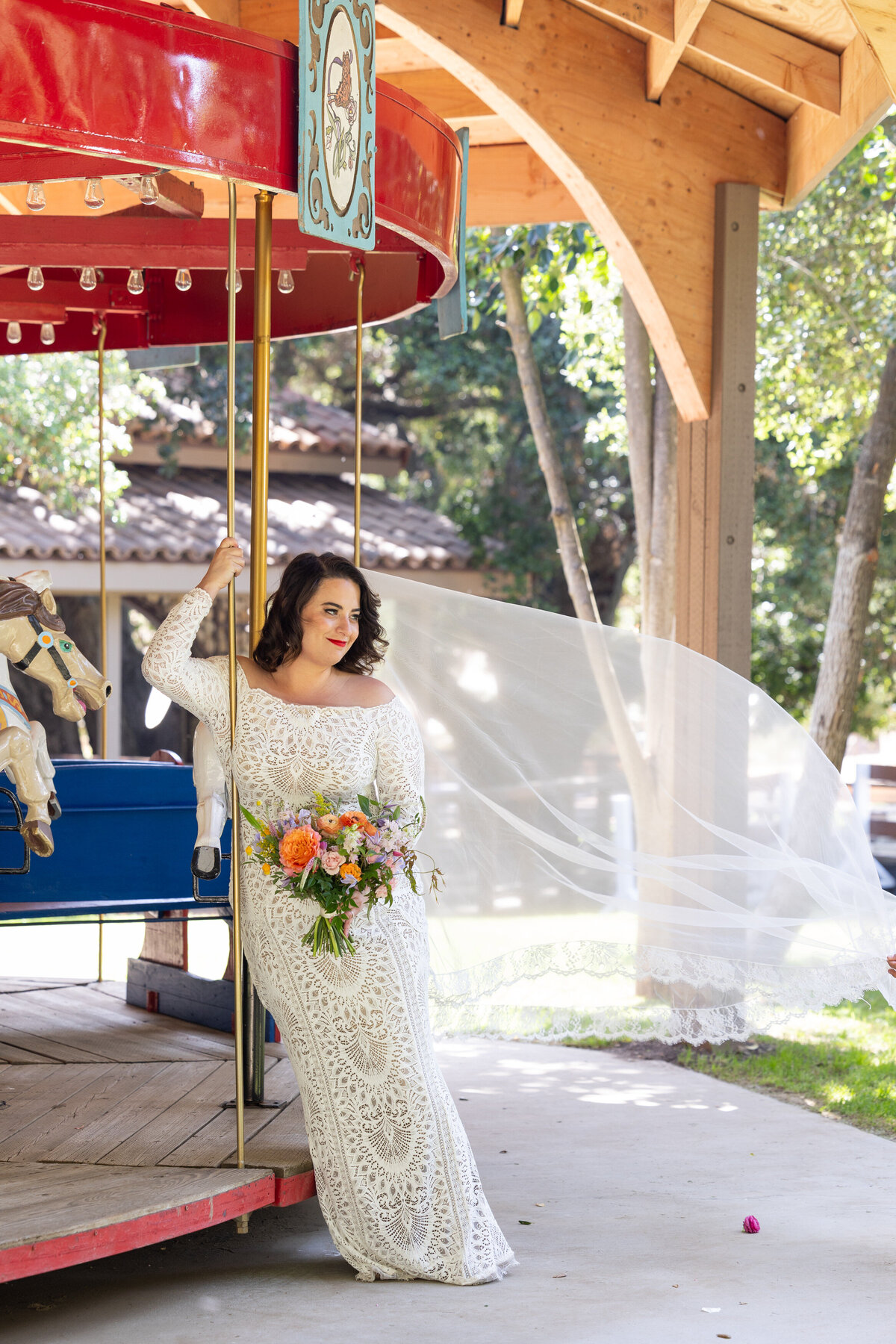 A bride leaning on a merry go round as her veil flys in the wind