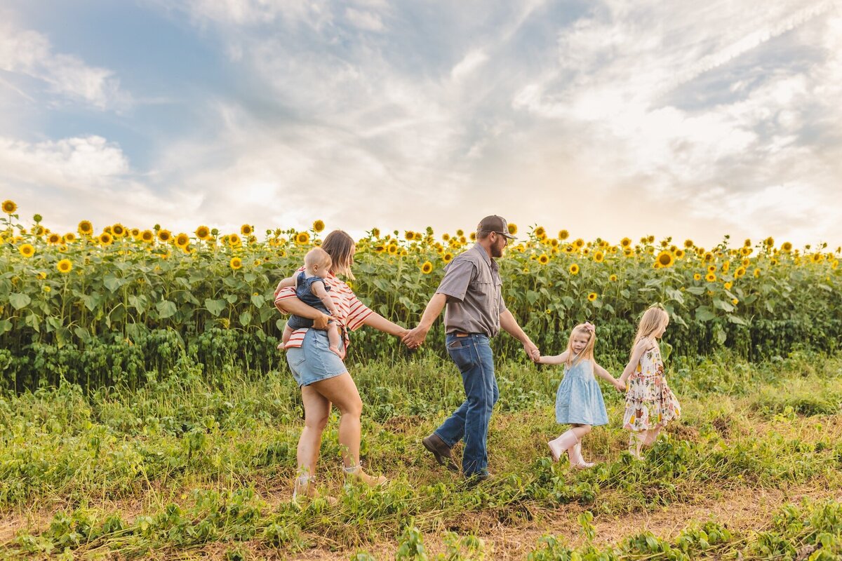 a family walking in a sunflower field while holding hands
