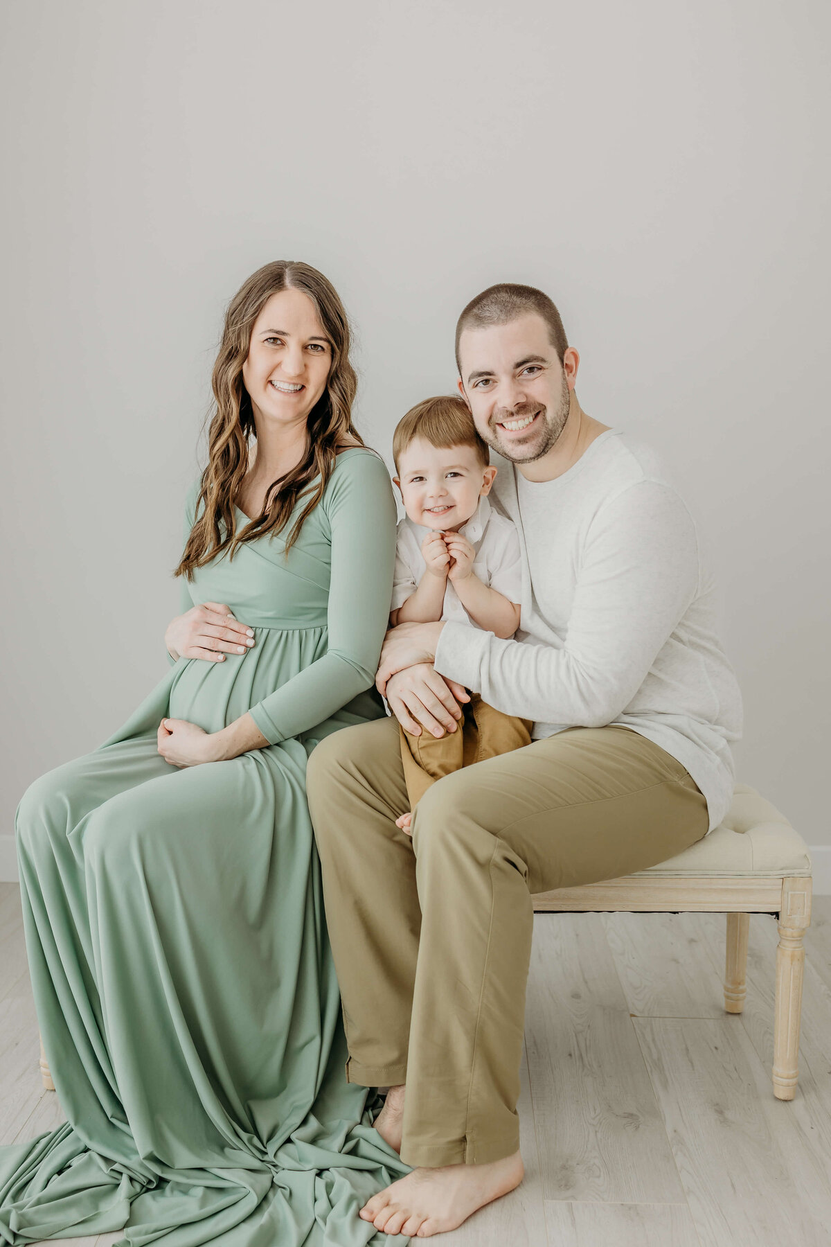Young family and mom holding belly pregnant in green dress smiling near Eau Claire, WI